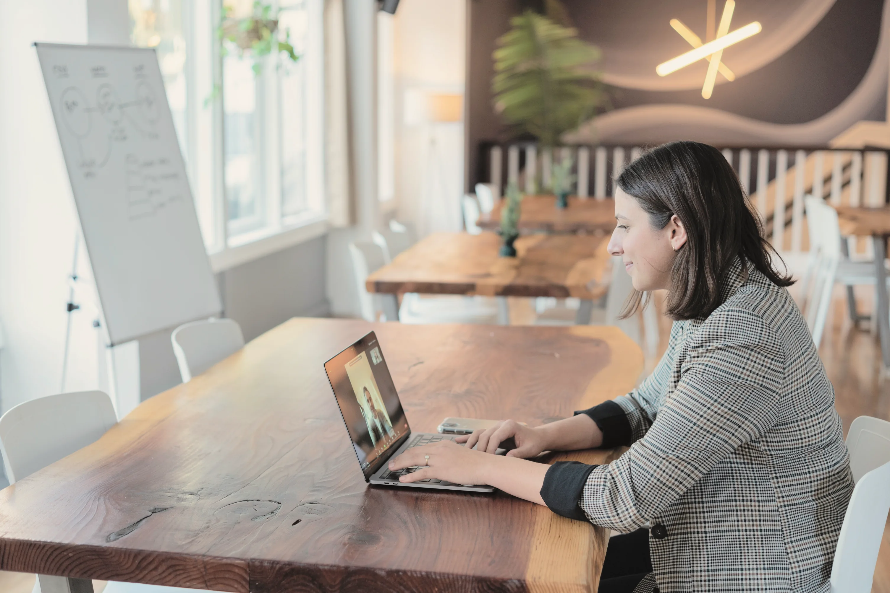 A mentor at a long wooden table smiles at her client, whose face is on her laptop screen